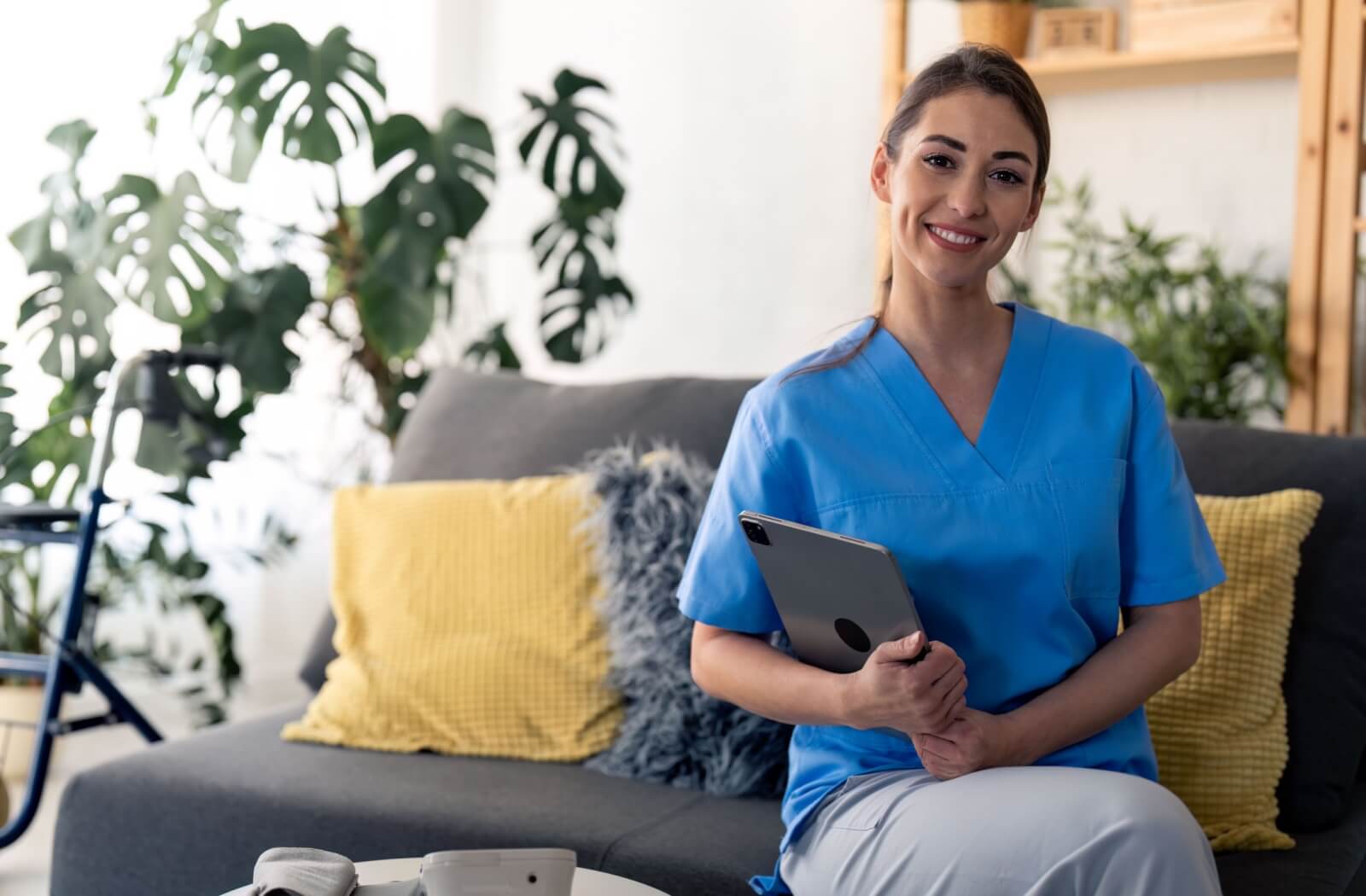 An assisted living nurse sitting on a couch while holding a tablet.