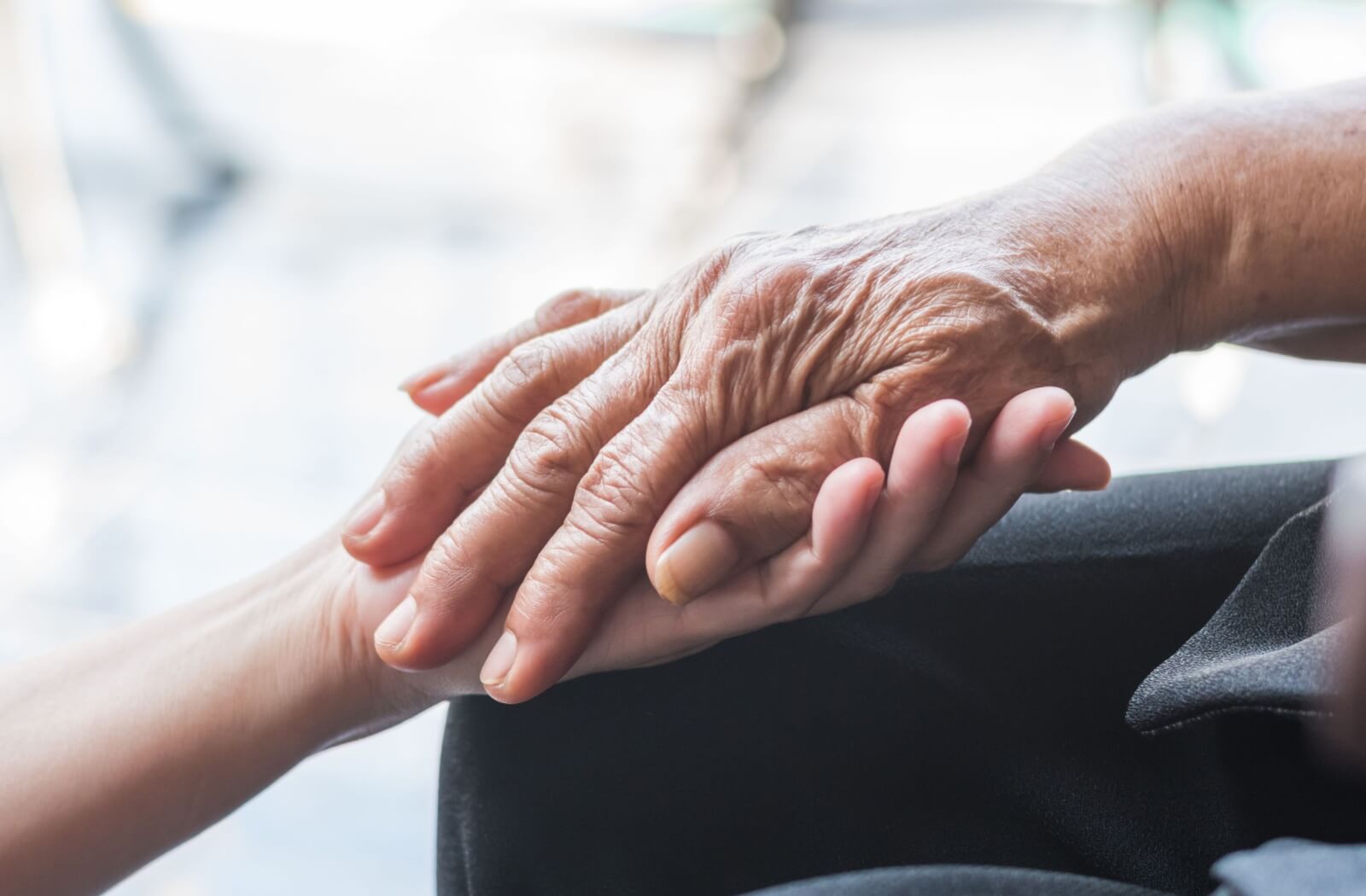 A close-up image of an adult child holding the hand of their aging parent.