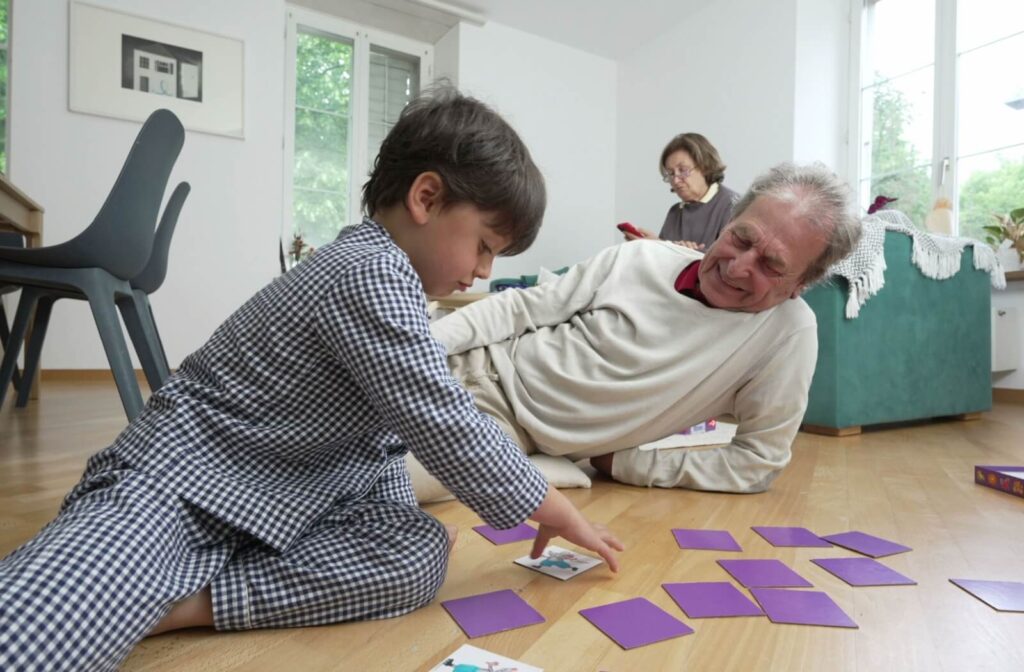 A senior plays a card matching game with their grandchild on the floor, both family members working on their memory